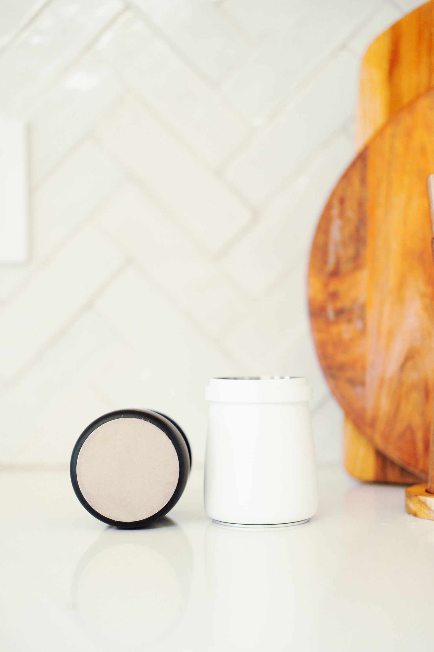 White and black jars sit on a marble counter with a wooden cutting board in the background.