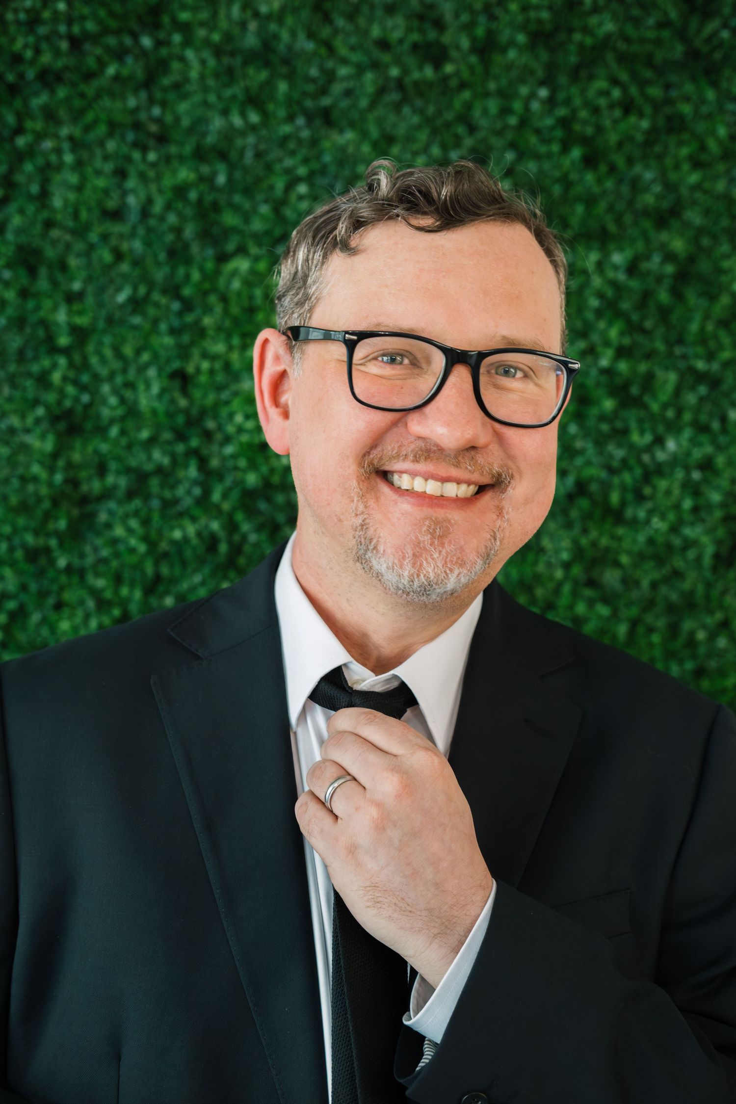 Professional headshot series with green hedge background showing friendly expressions in formal attire.