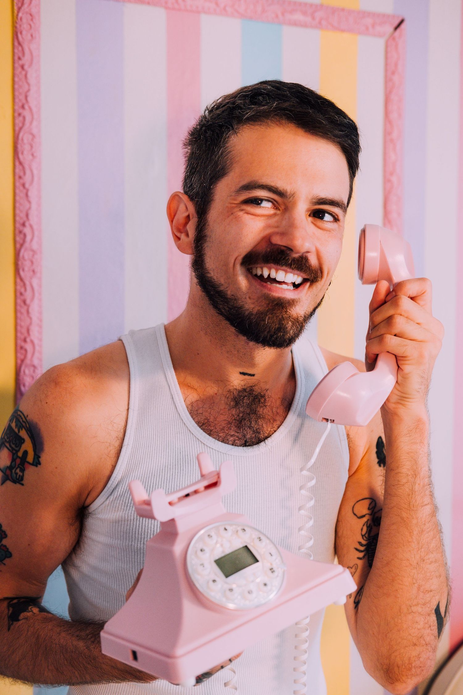 Queer consultant headshot, brightly colored & creative. They're holding a pink phone with a striped backdrop in a SF personal branding shoot