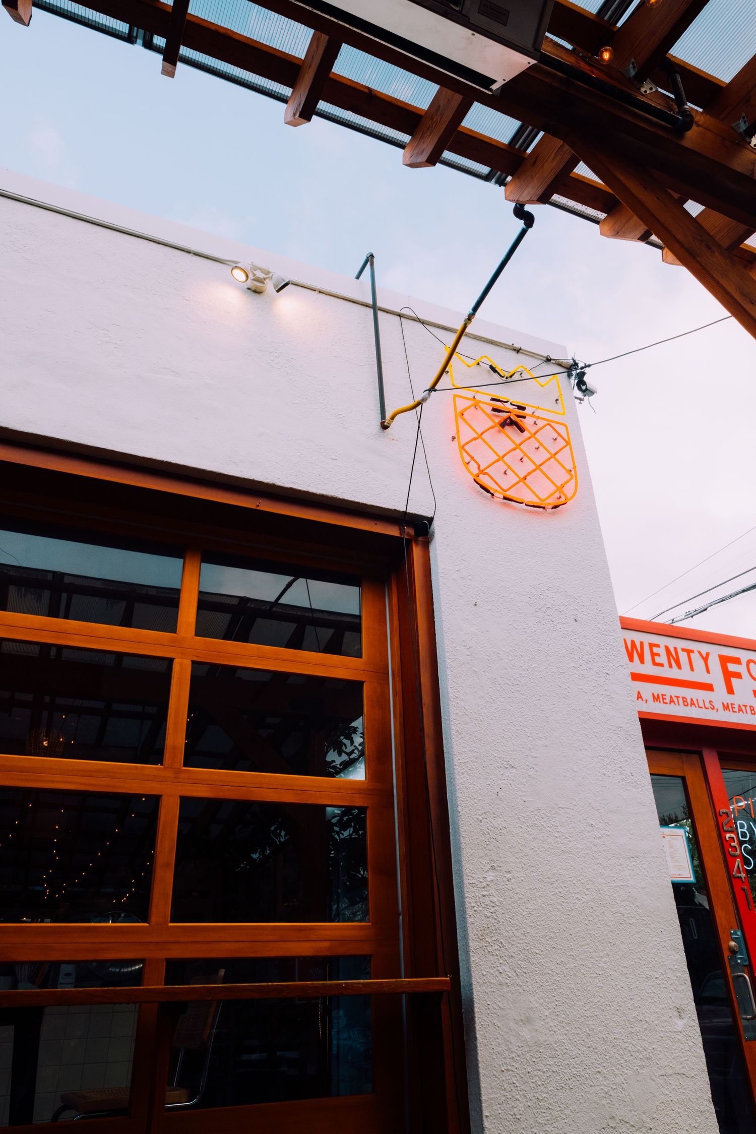 Modern storefront exterior with wooden beams and a decorative orange neon light fixture.