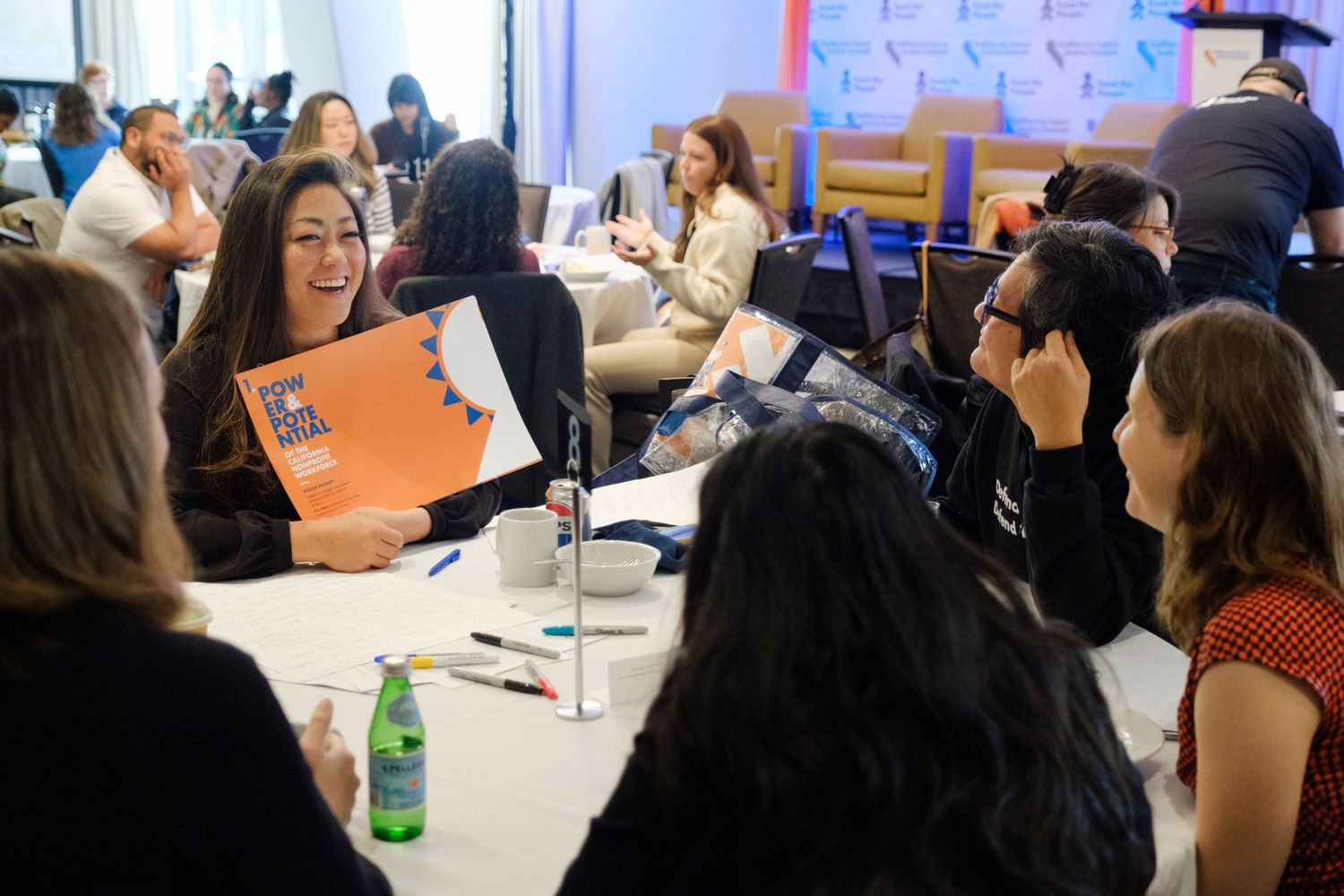 Diverse group collaborating at workshop tables during professional development event with conference banners visible.