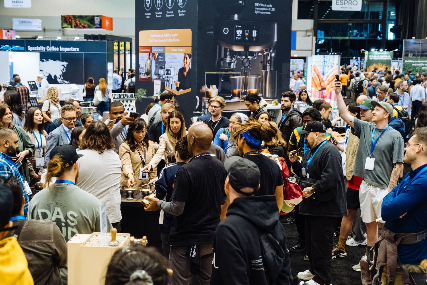 A crowded scene at a trade show or convention with people gathered around vendor booths and displays.