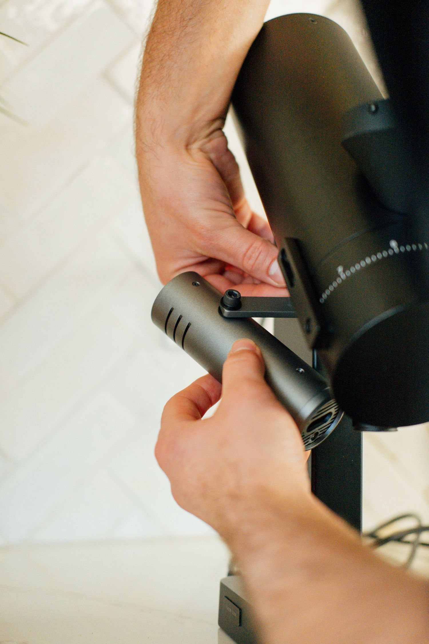 Hands adjusting settings on a black cylindrical coffee grinder.