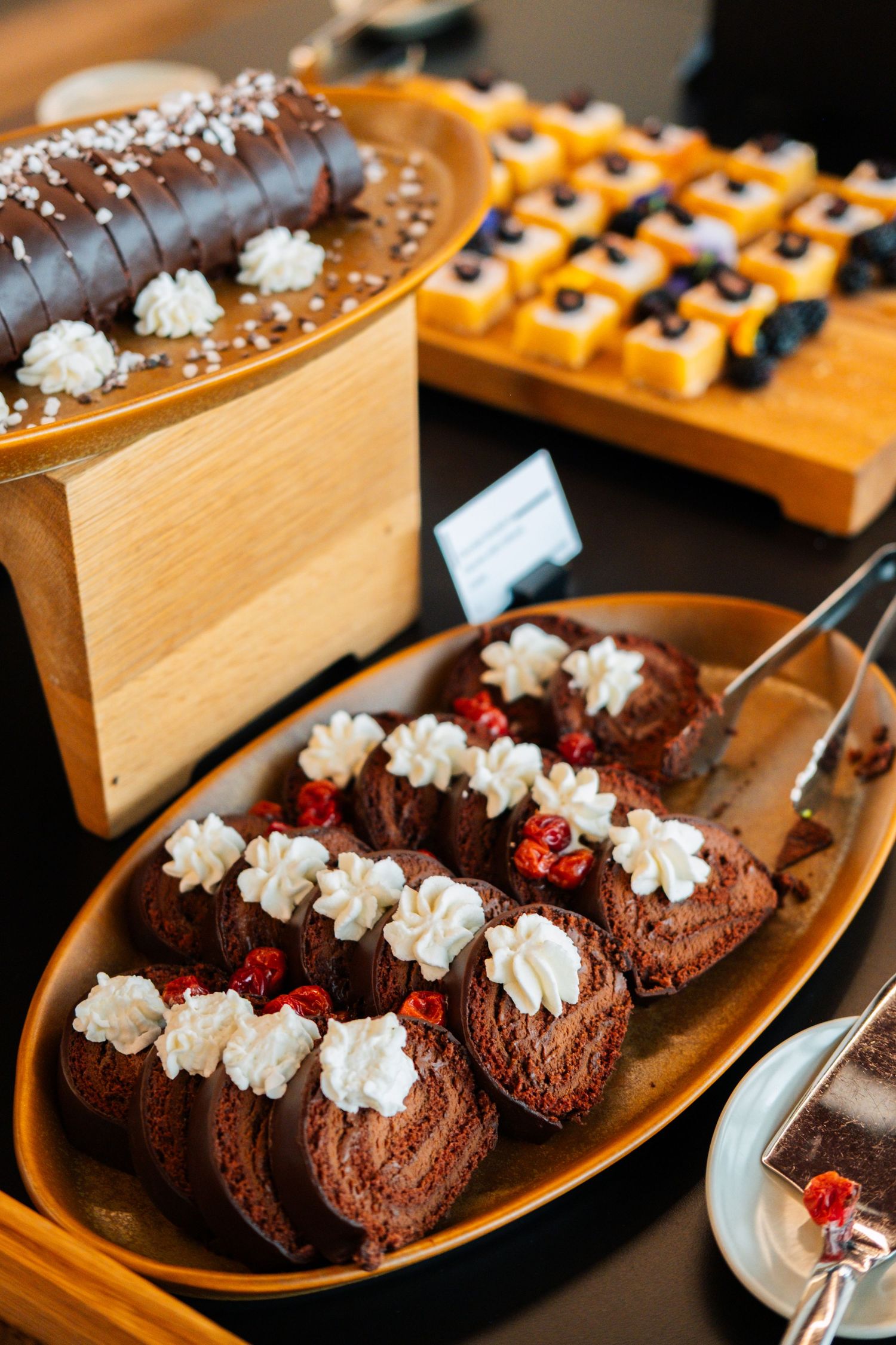Elegant chocolate desserts decorated with whipped cream and berries on wooden serving platters at a buffet display.