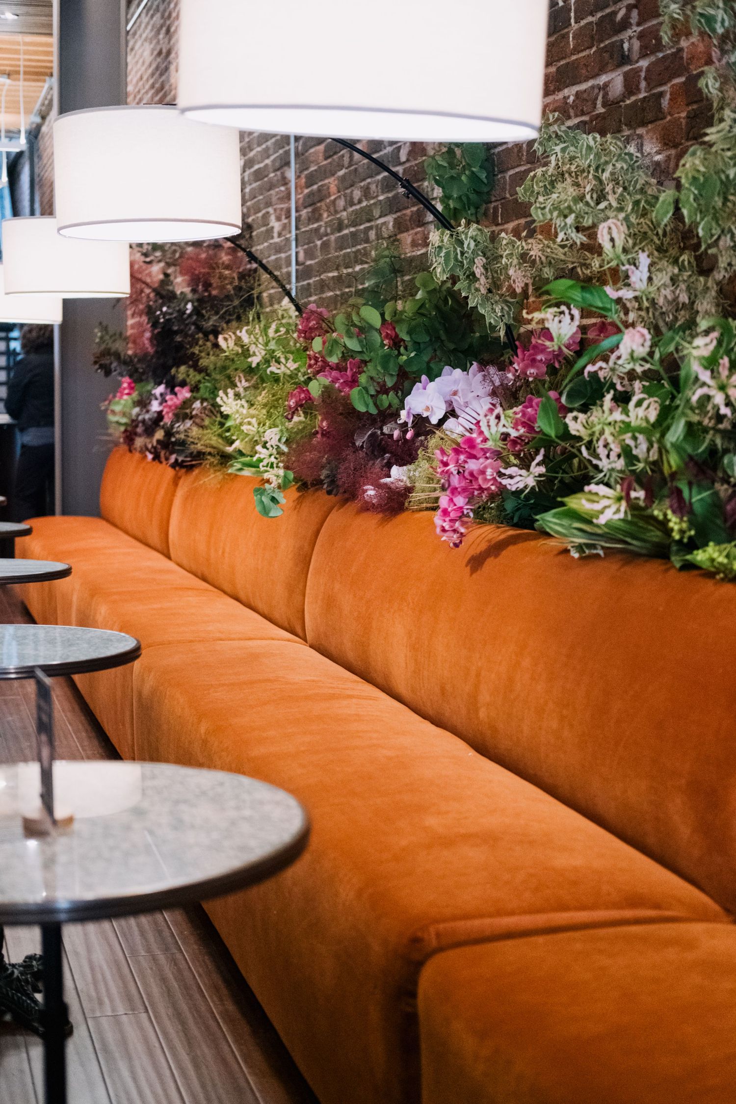 An elegant restaurant booth with orange velvet seating decorated with colorful floral arrangements.