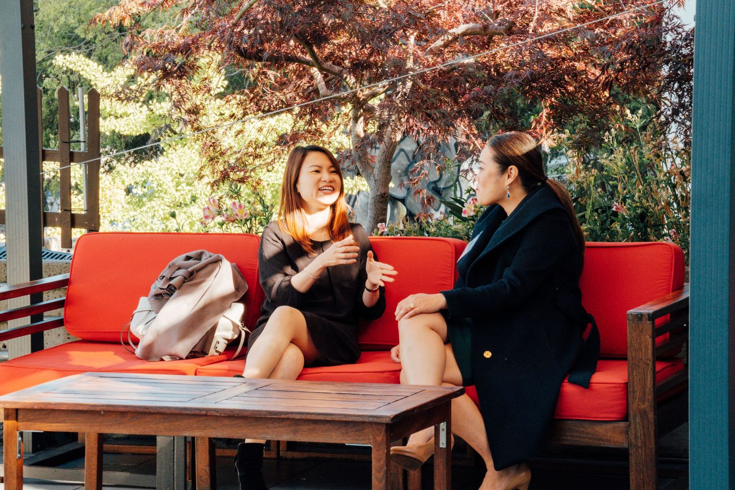 People relaxing on red cushioned benches under autumn foliage.