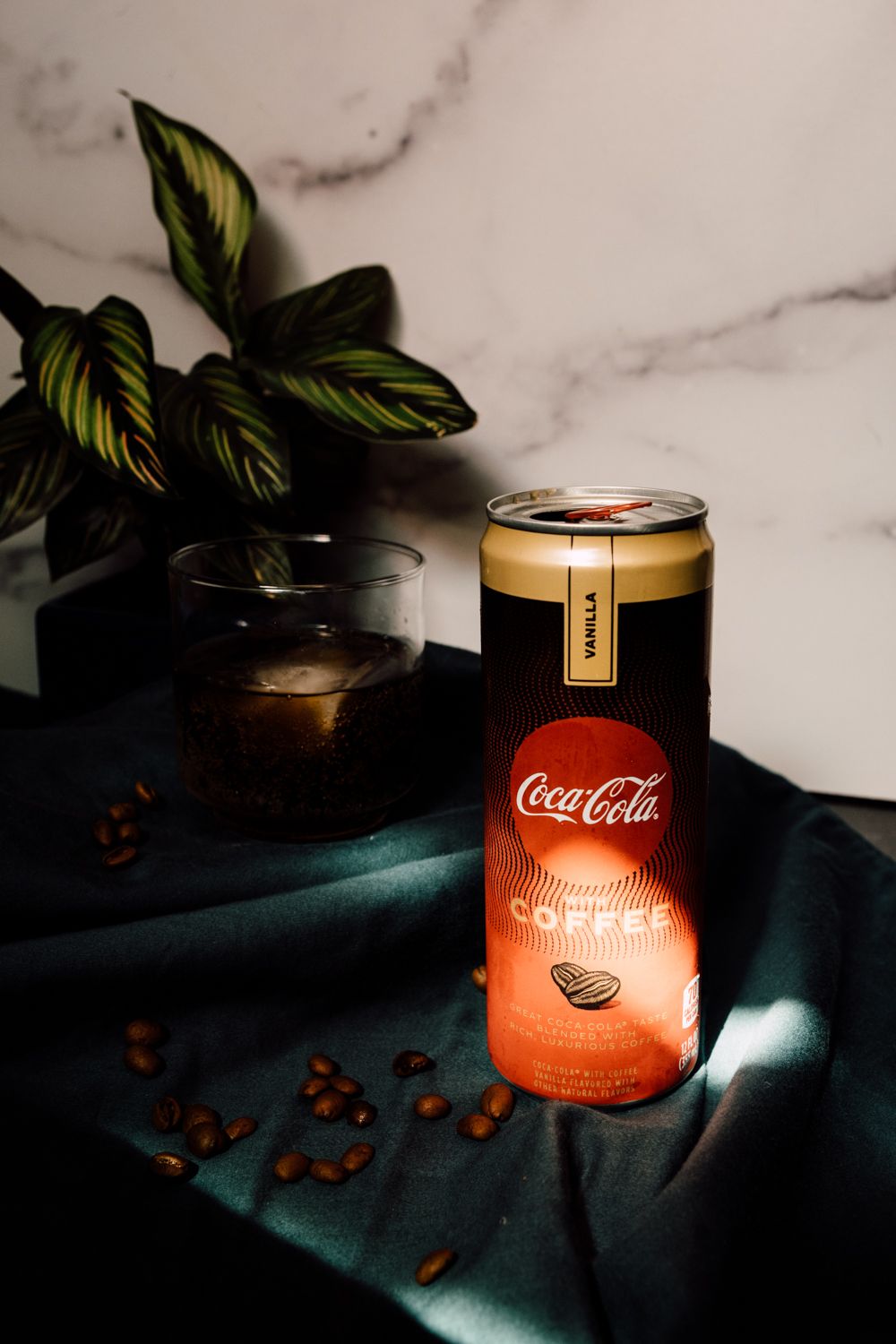 Coca-Cola coffee drink can with coffee beans on dark fabric against marble background.