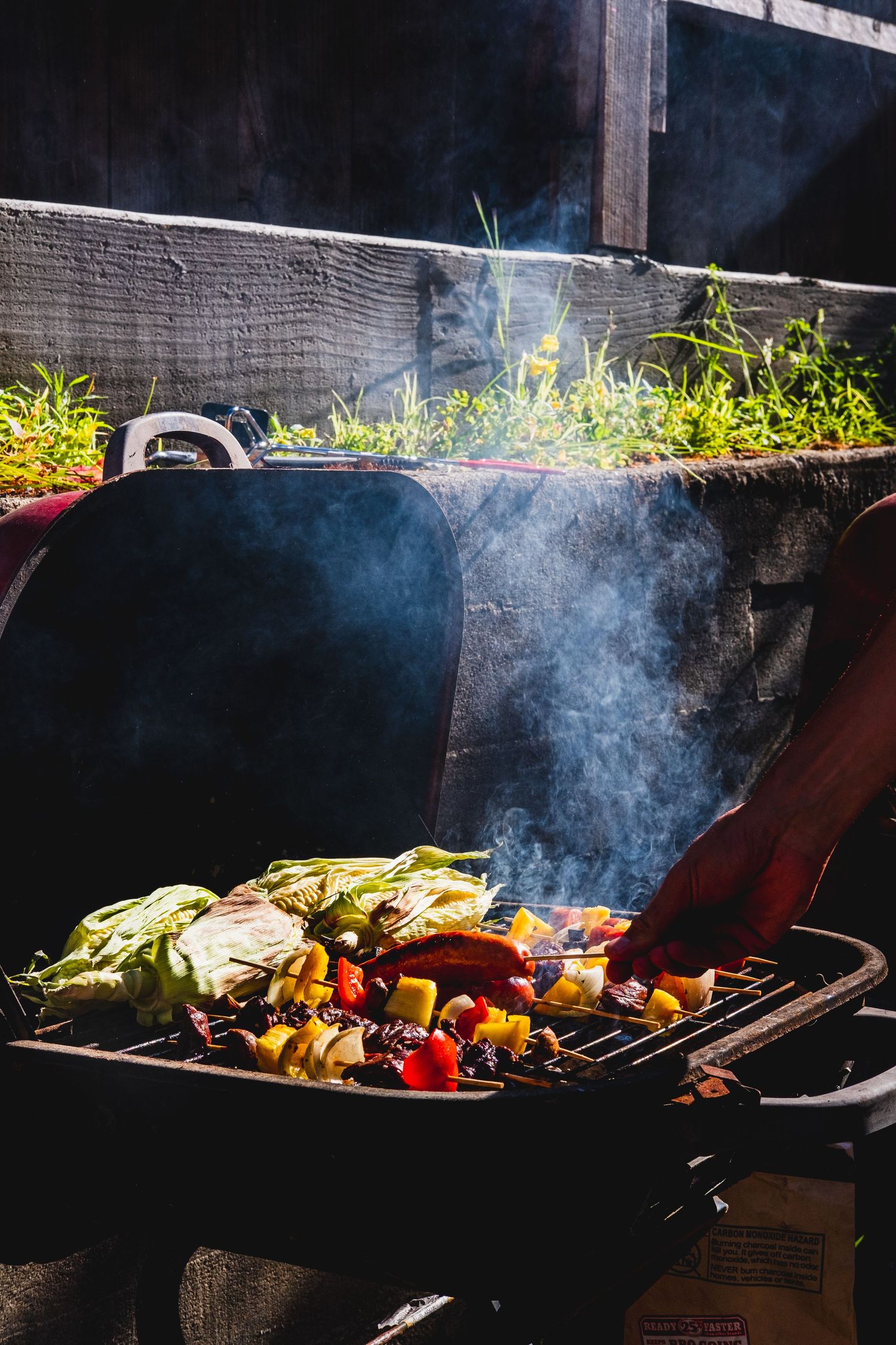 Colorful vegetables and kabobs cooking on a smoky outdoor grill with steam rising in dramatic lighting.