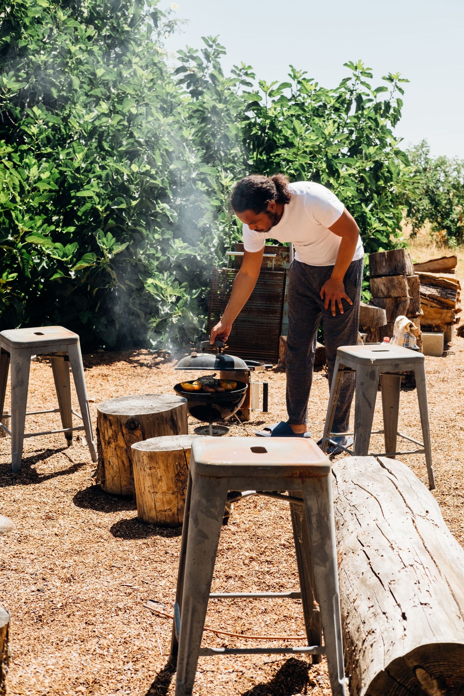 Person tending to a smoker grill in an outdoor garden setting.