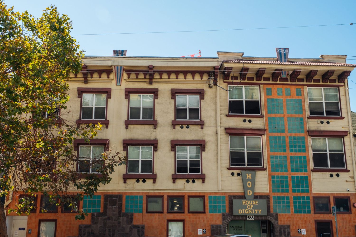 Historic brick apartment building with ornate cornice details and turquoise-framed windows along a city street.