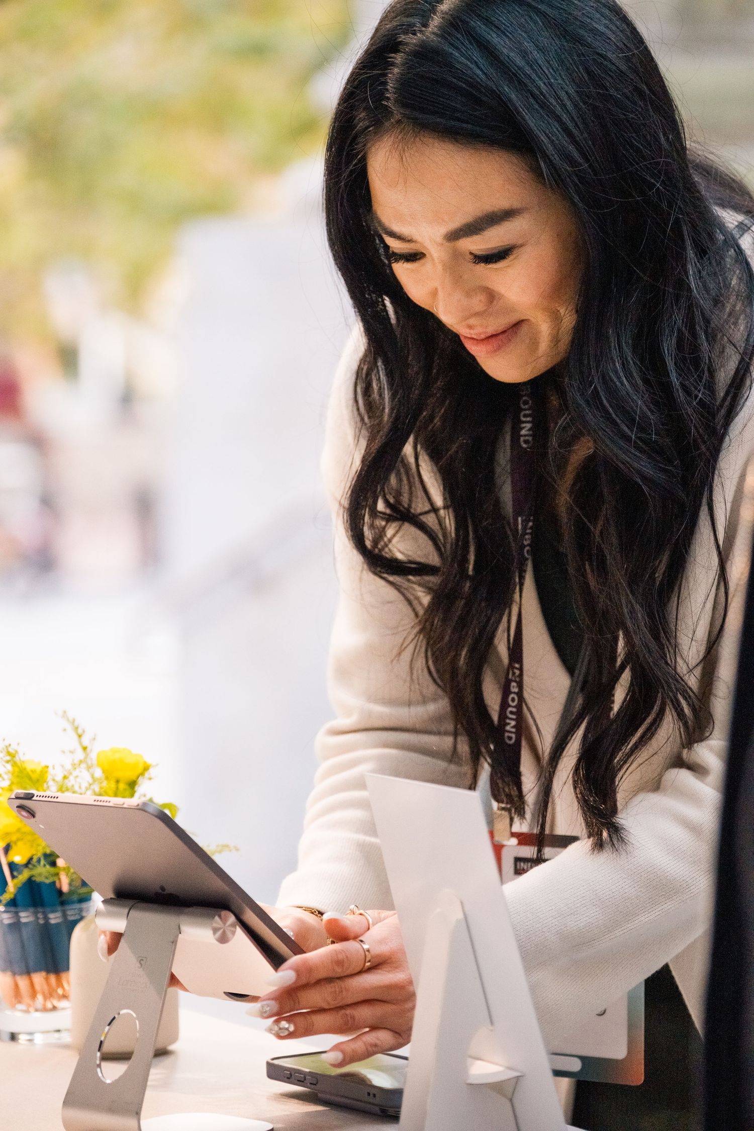 Person wearing white blazer writes in notebook with flowers in a modern cafe setting at desk.