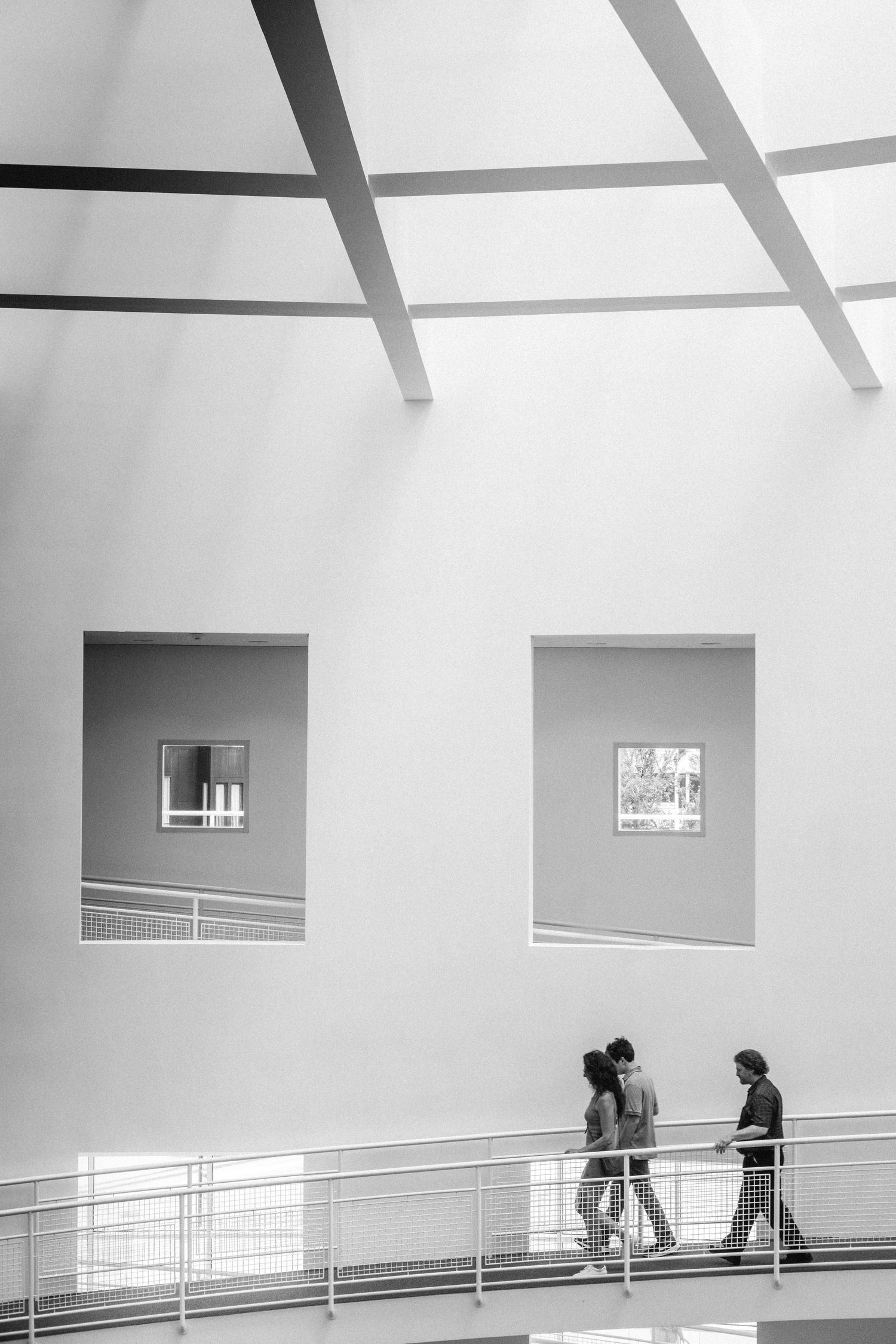 Abstract architectural image showing minimalist white interior spaces with angular beams and people walking along railings.