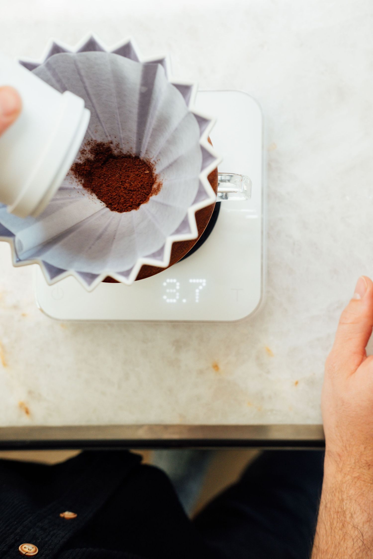 Coffee grounds being poured into a paper filter on a digital scale.