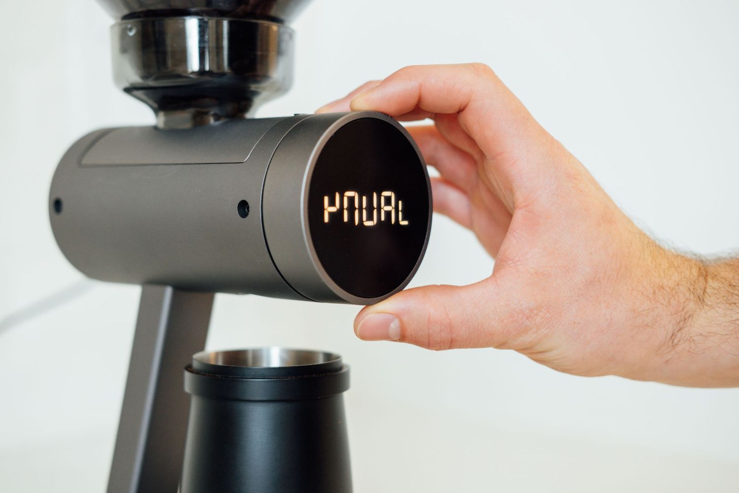 Hand adjusting digital display on modern coffee grinder.