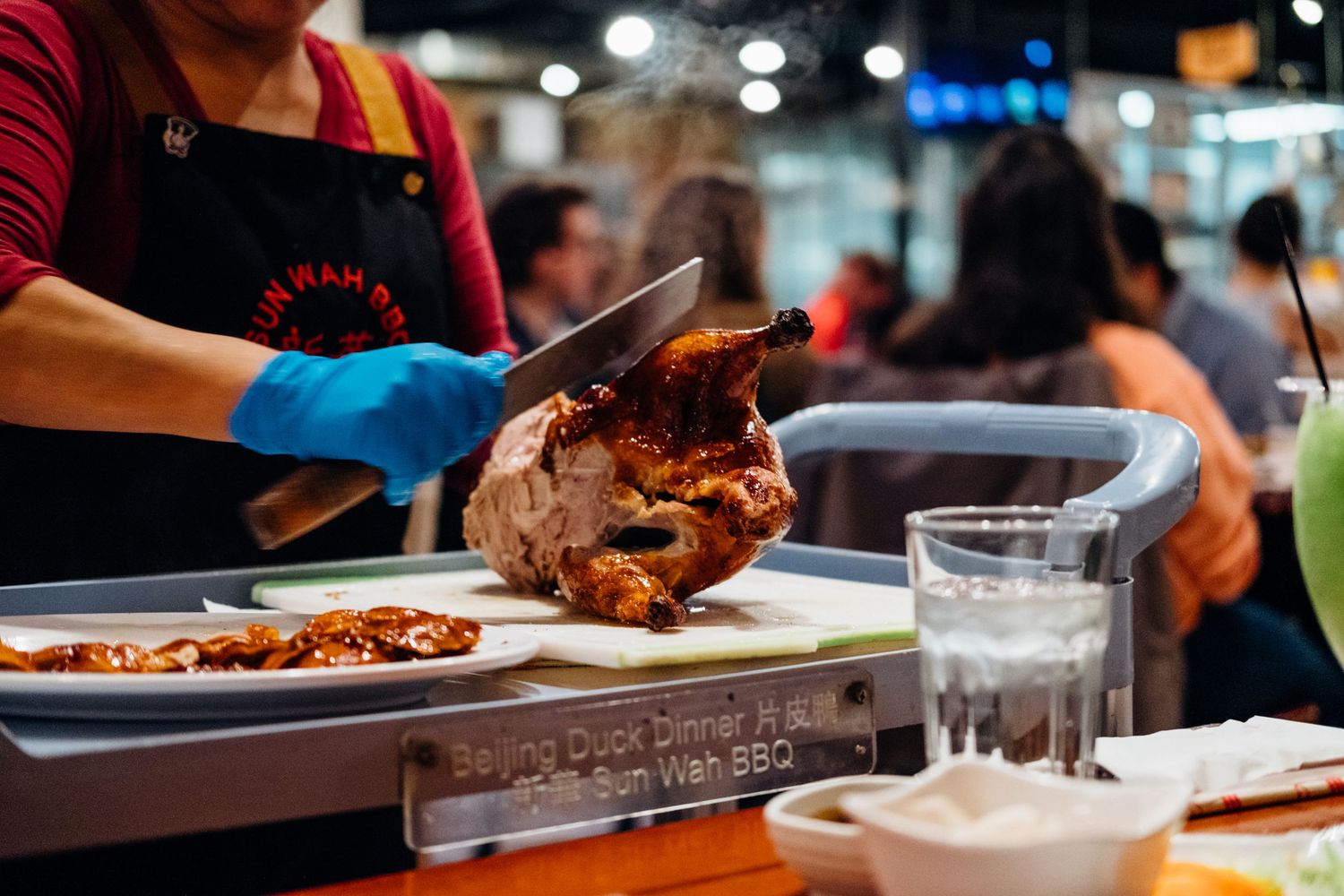 Chef in red and black prepares a roasted chicken dish in a busy restaurant kitchen.