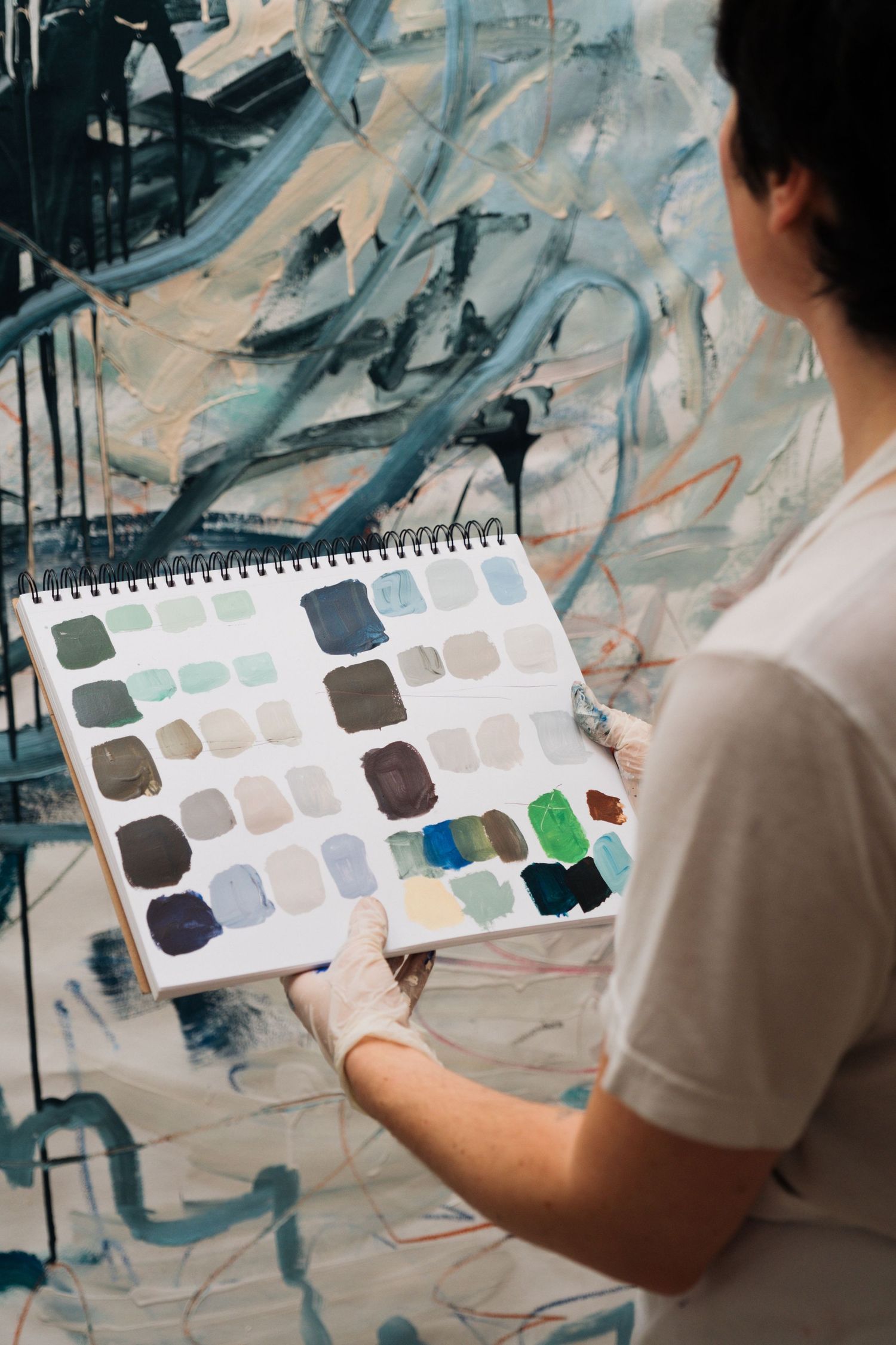 Artist holding a color swatch palette against an abstract blue and white painting background.