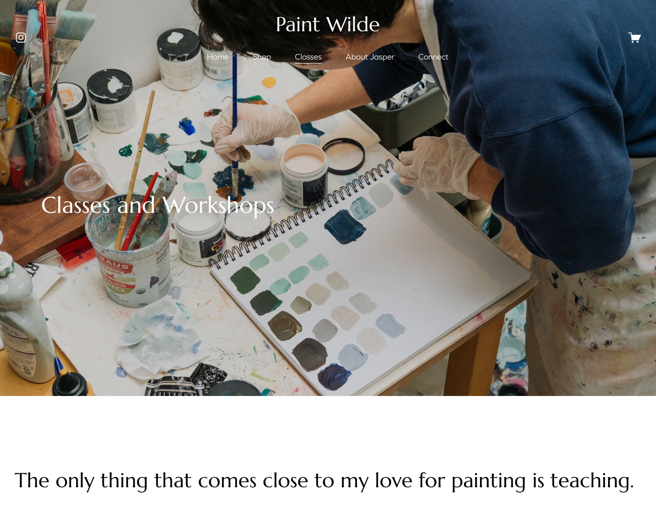 Artists work with watercolor paint swatches and supplies on a light wooden surface in a creative studio setting.