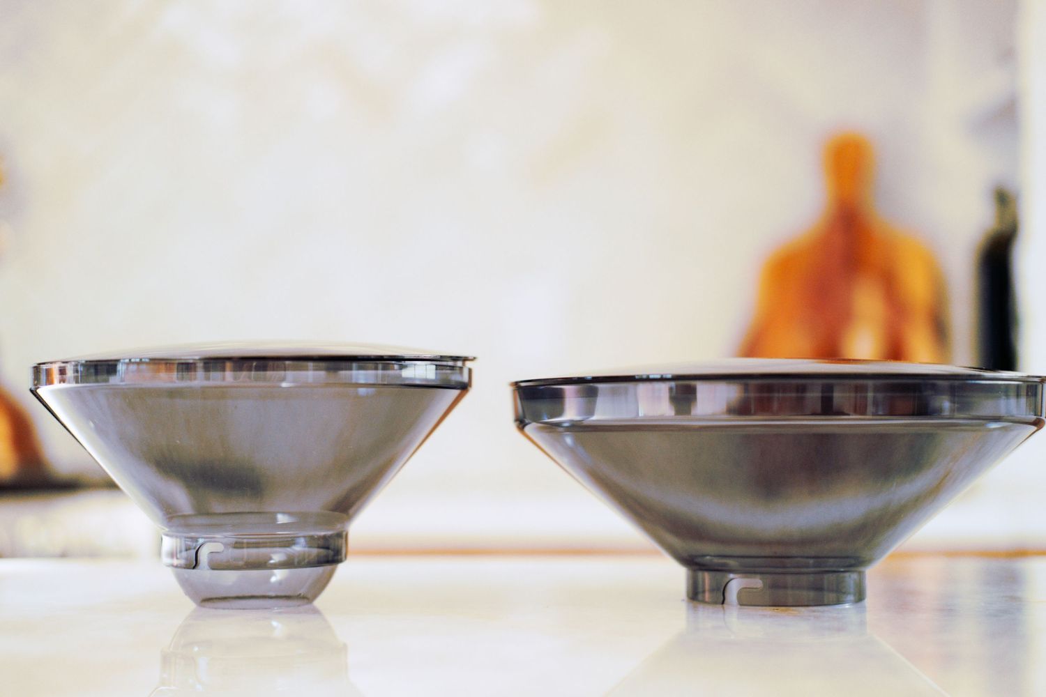 Two metal conical coffee filter holders displayed on a light colored countertop.