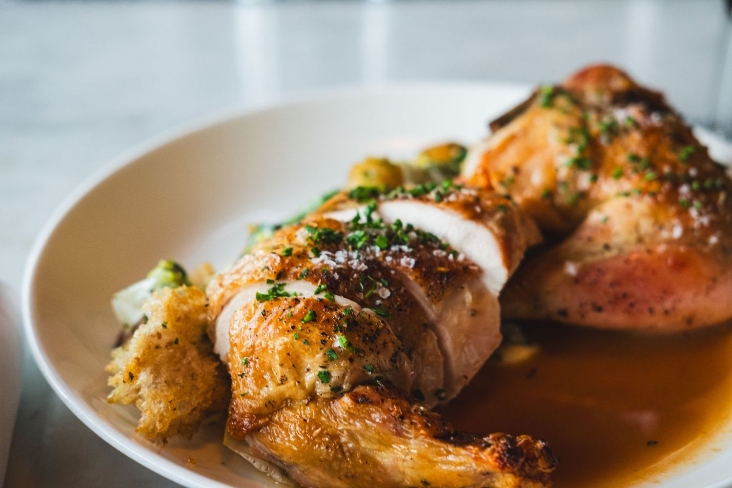 Golden roasted chicken pieces garnished with fresh herbs and served in a savory sauce on a white plate.