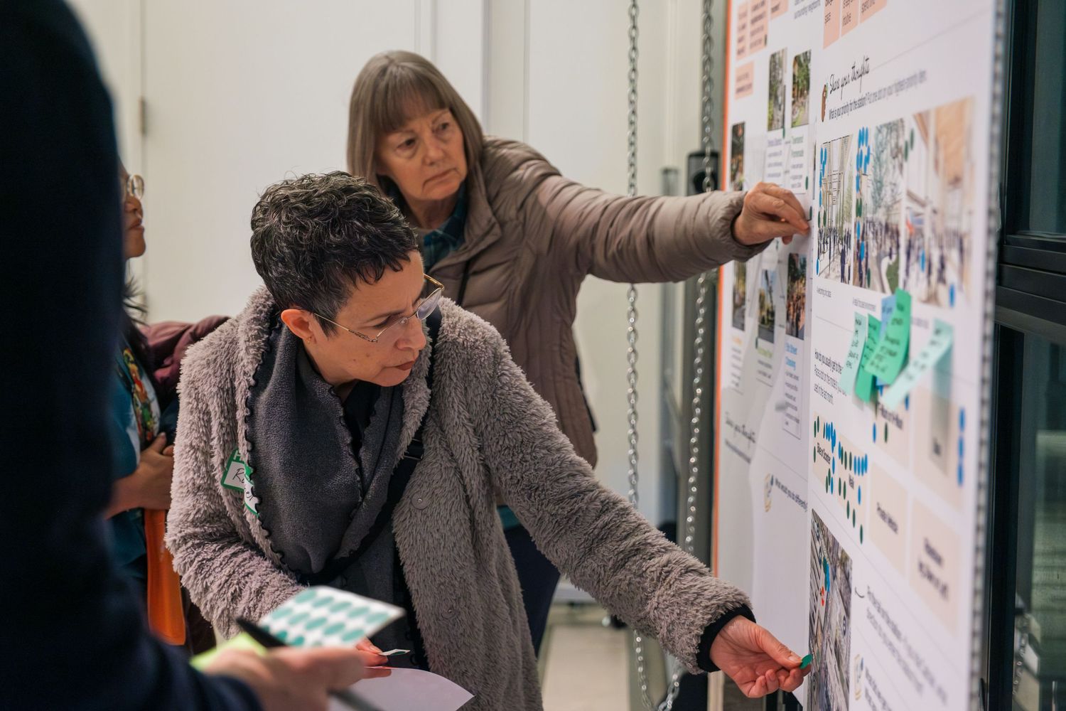 People examining and discussing content posted on a wall during a meeting or presentation.