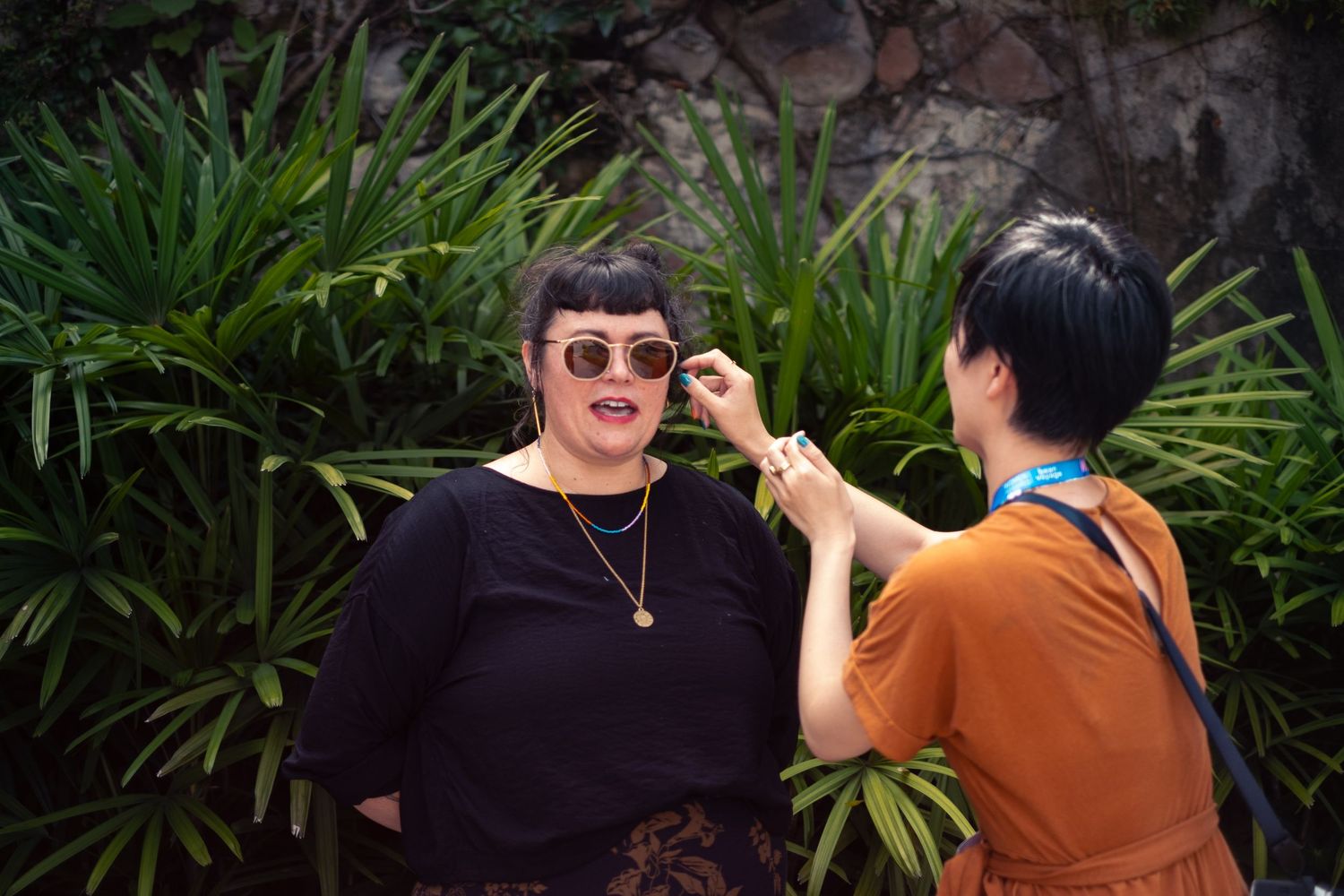 Two people interact in front of lush tropical foliage in a candid moment.