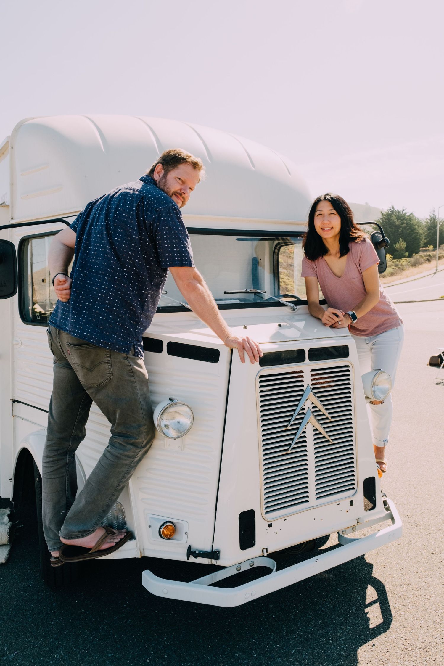 Couple posing with vintage white food truck on sunny day.