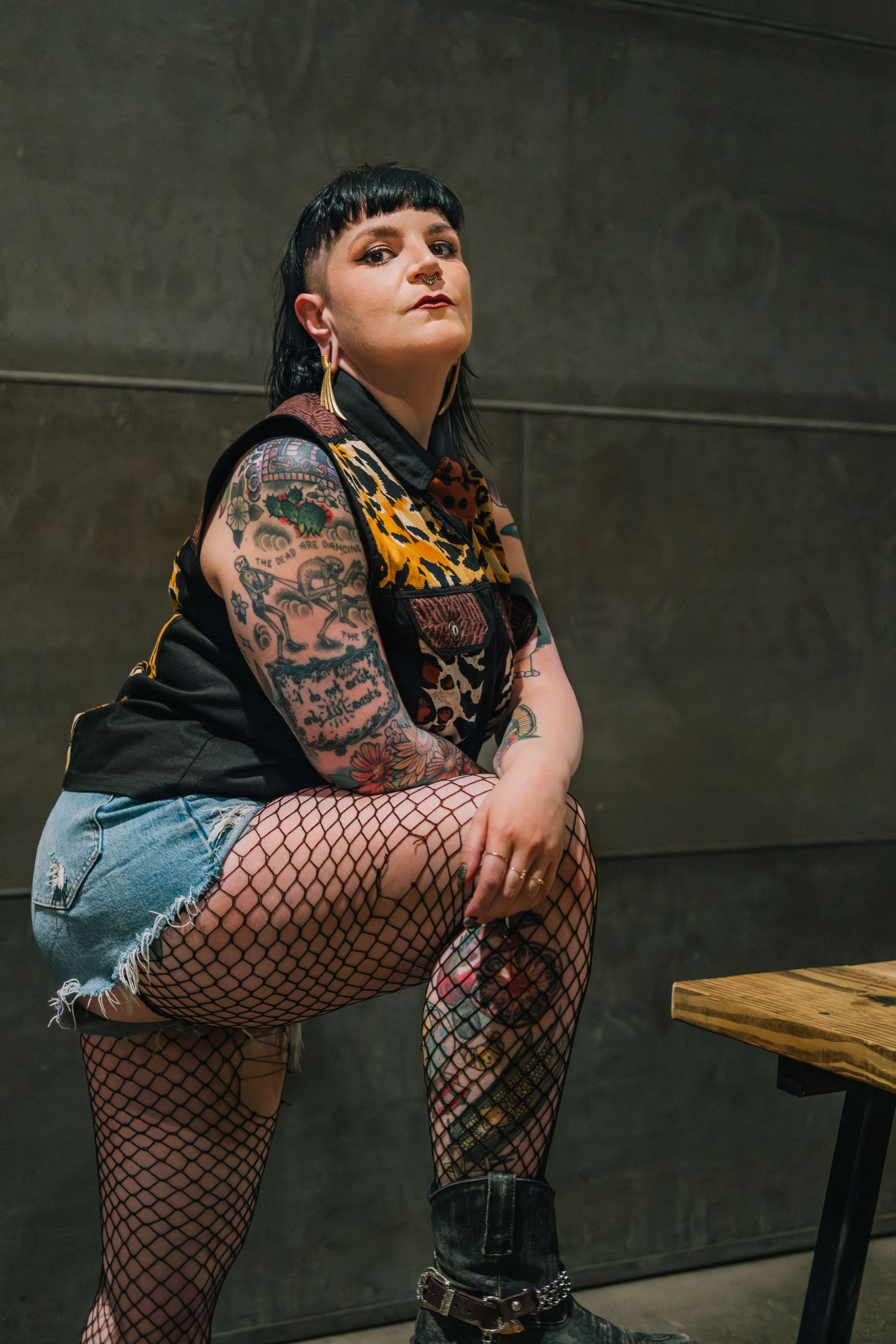Alternative fashion model in fishnet stockings and denim strikes dynamic poses against dark industrial backdrop.