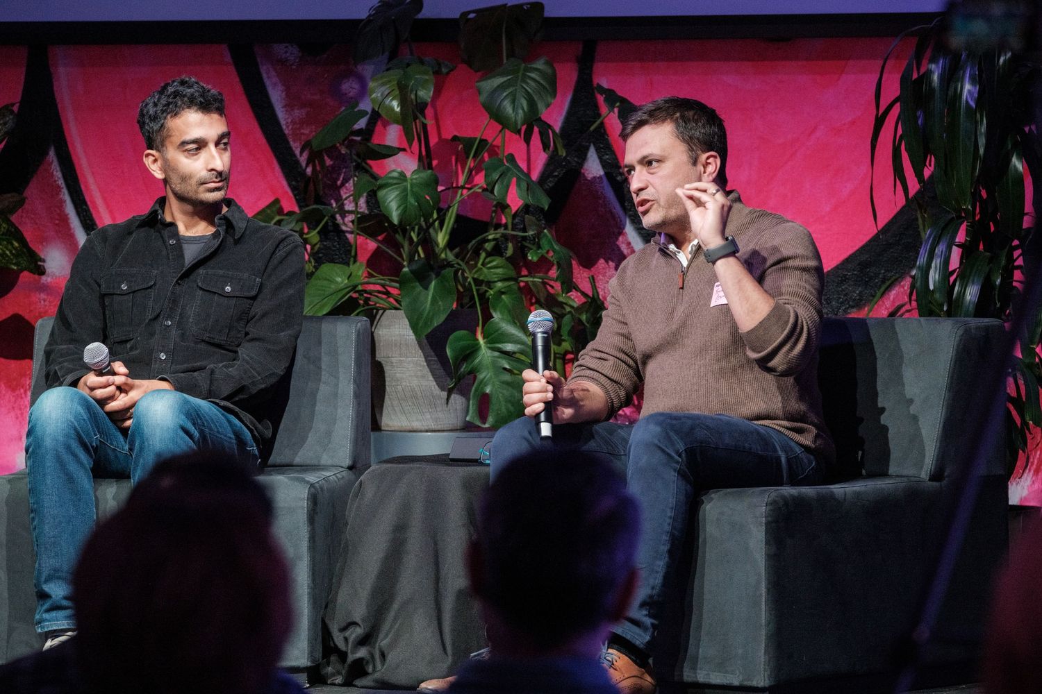 Two speakers engaged in conversation while seated on stage with pink backdrop.