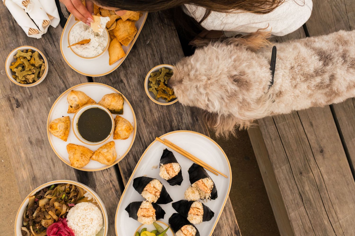Overhead view of a rustic brunch table setting with coffee cups, pastries and fresh flowers on wooden surface.