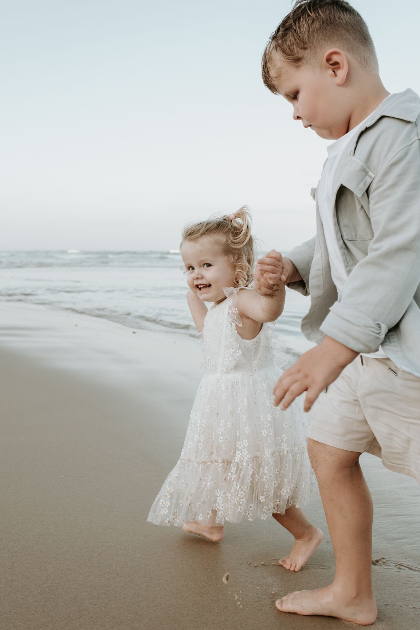 Two children in light colored clothing playing and laughing together on a foggy beach.