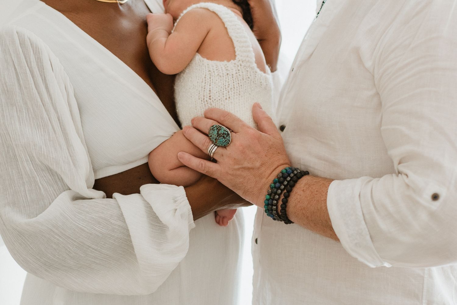 Close-up of hands wearing a turquoise ring and leather bracelet against white clothing.