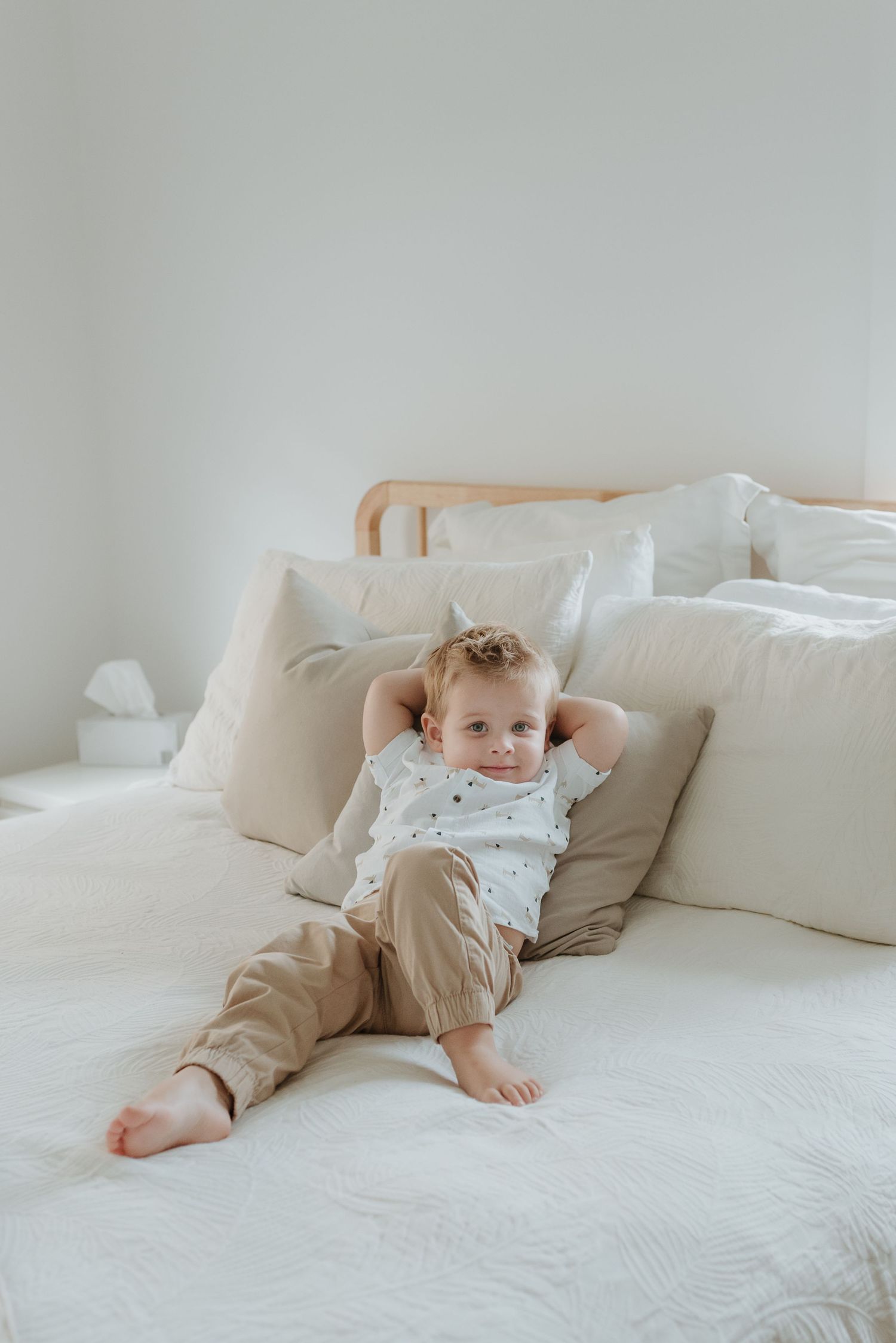 Baby in soft neutral-colored clothing lying on white bedding shows gentle progression of movement while rolling over.