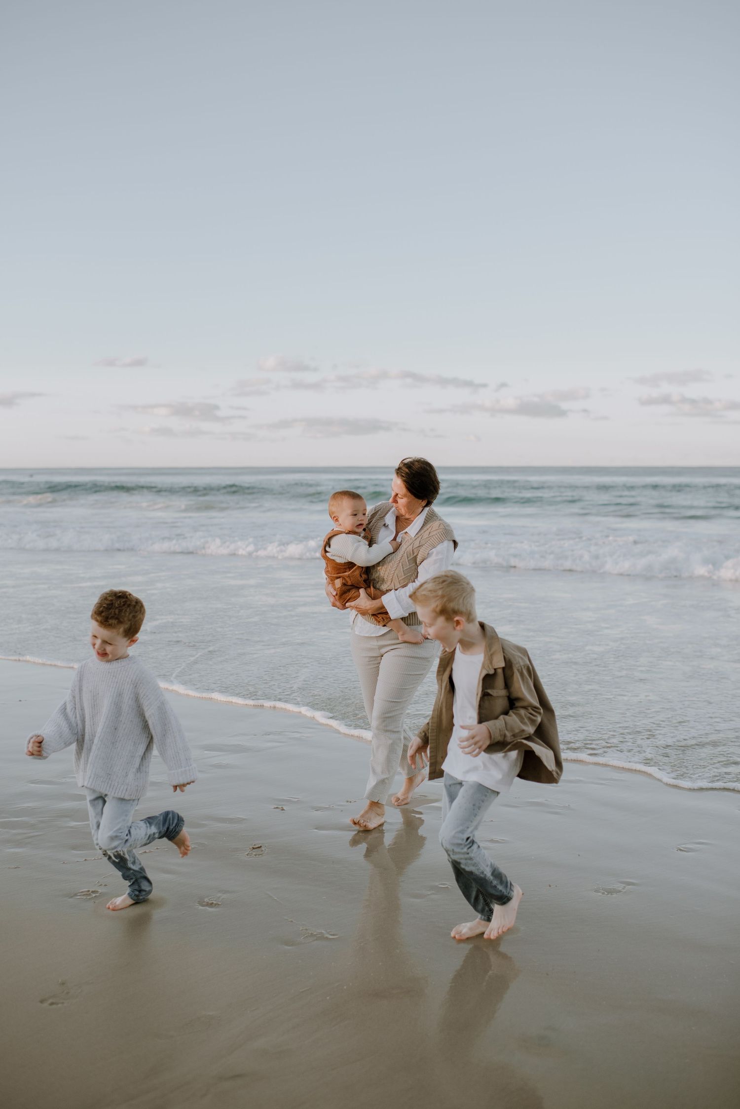 A family runs and plays together along a misty beach shoreline at sunset with gentle waves in the background.