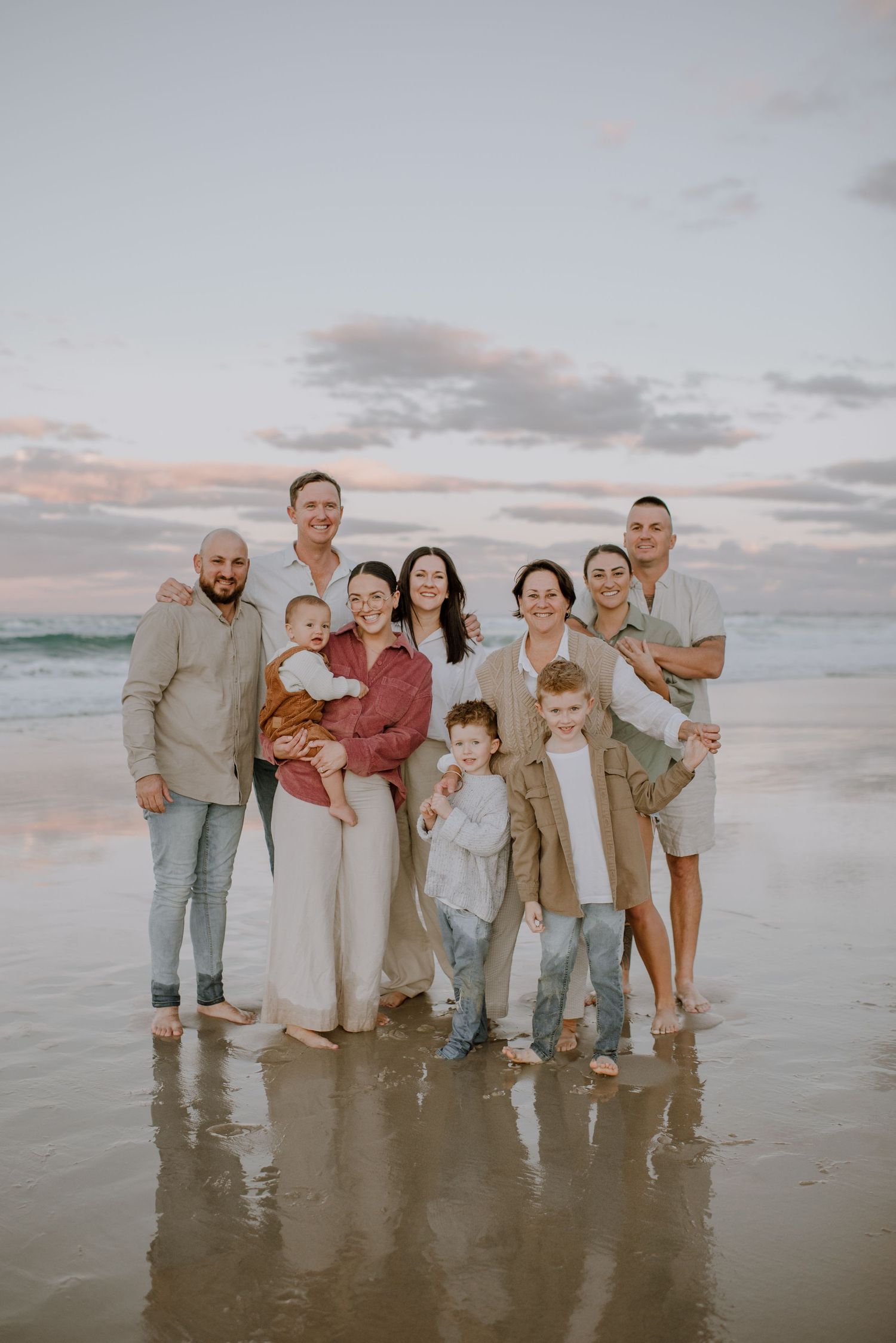 Group stands together at sunset on a beach with waves and cloudy sky in the background.