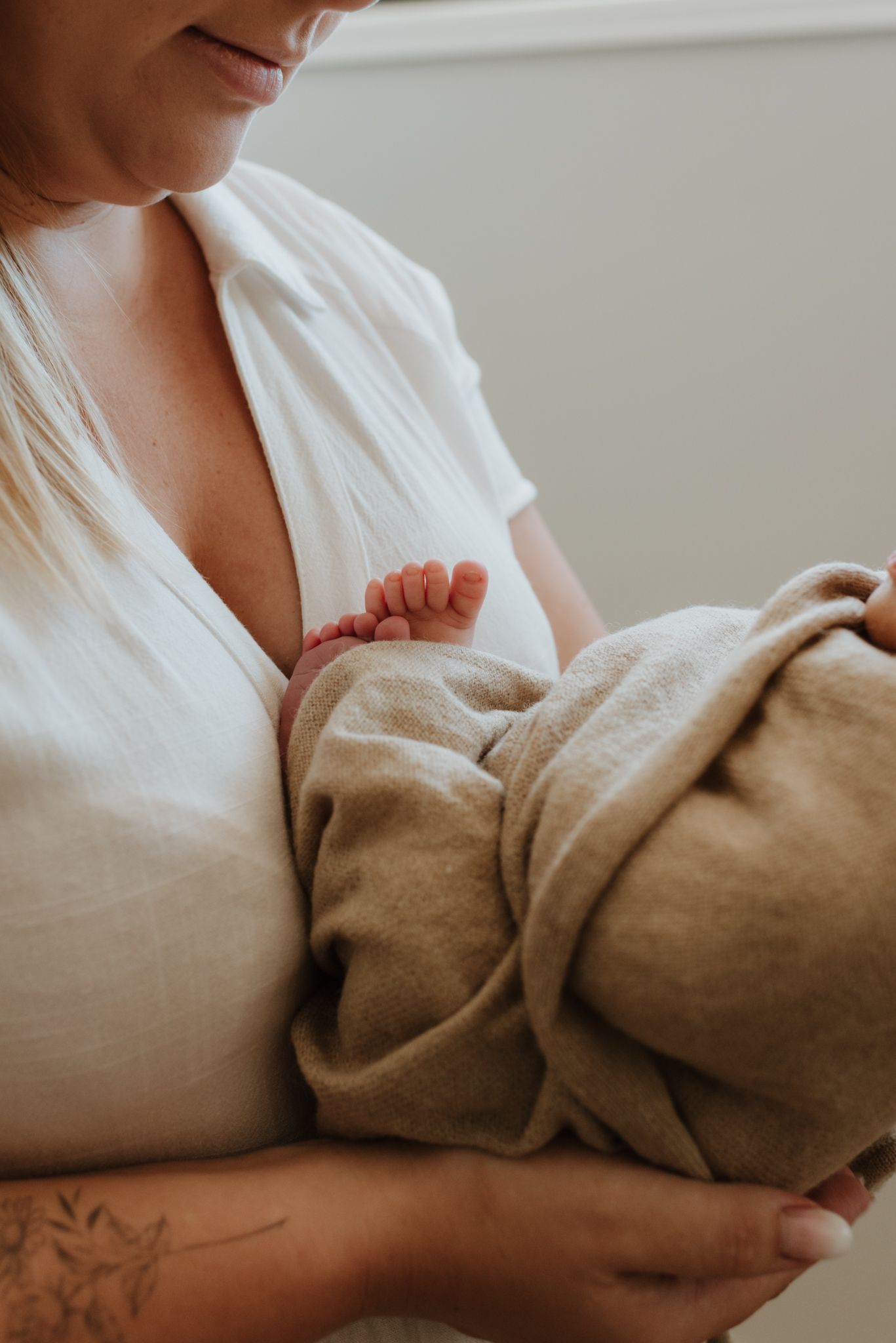 A tender moment showing a baby's tiny foot while being cradled in a soft beige blanket against white clothing.