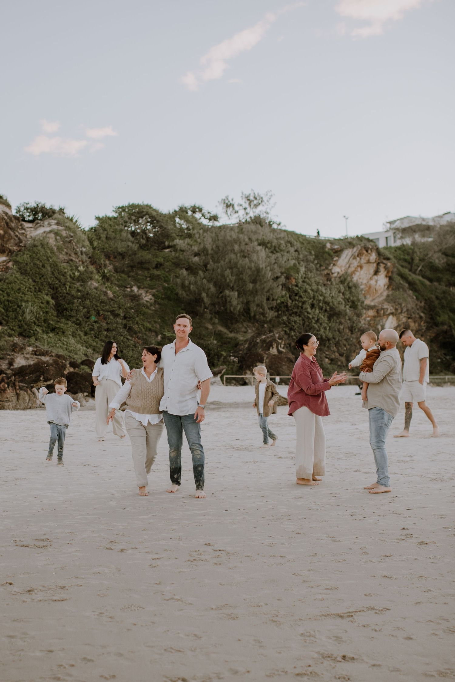 A group of people walking together on a sandy beach with greenery and trees in the background during daytime.