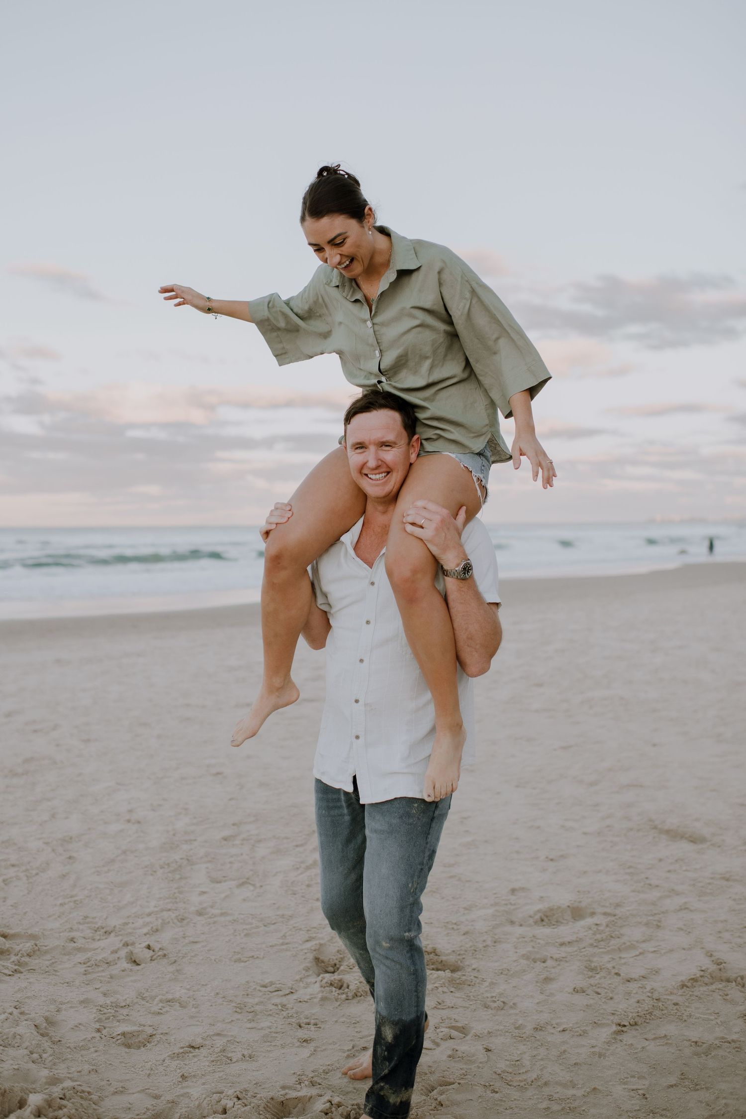 Two people enjoy a playful moment on the beach at sunset with one giving a shoulder ride to the other.