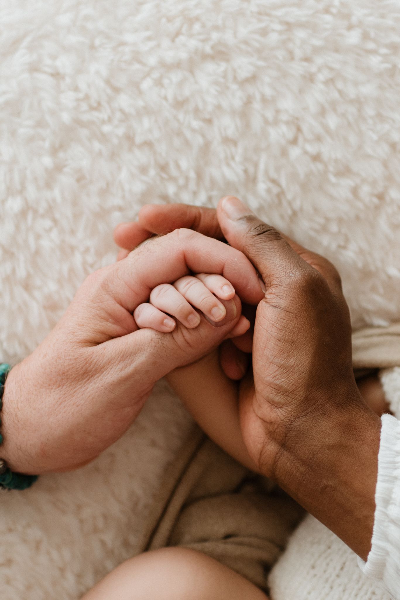 An intimate close-up of two hands gently holding each other against a soft white textured background.