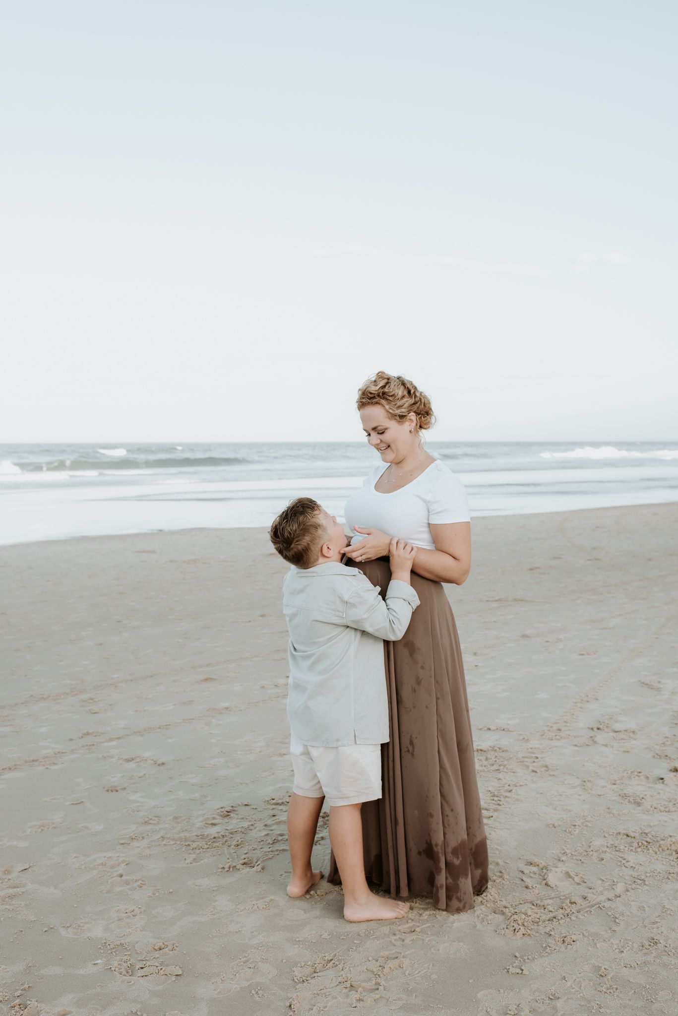A heartwarming moment shared between two people in white outfits standing together on a serene sandy beach at sunset.