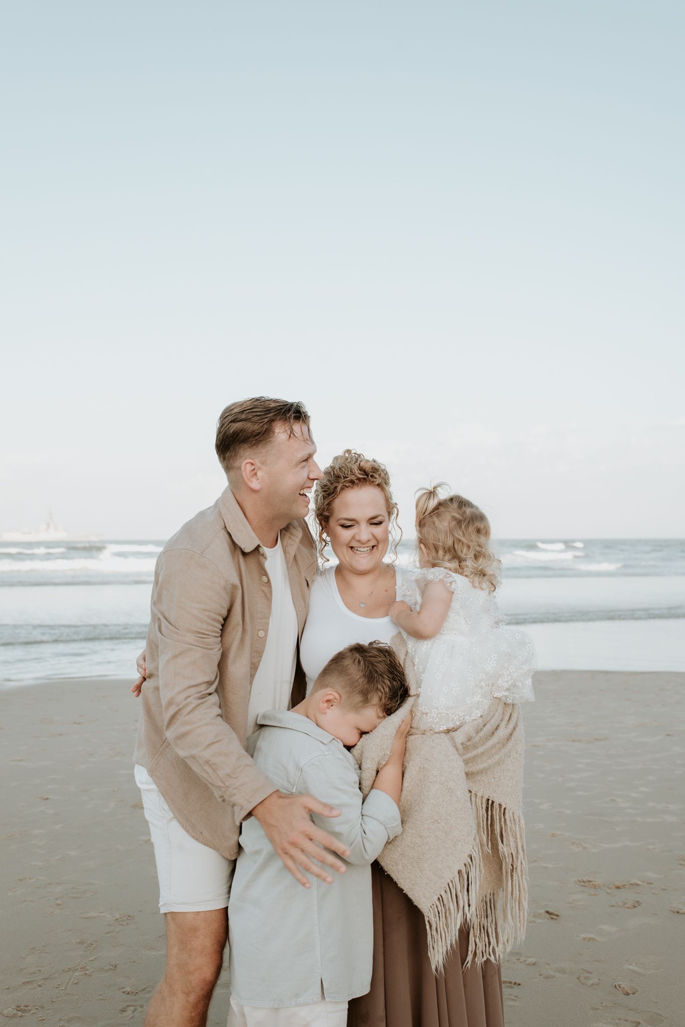 A family shares an intimate embrace on a peaceful beach with ocean waves in the background.