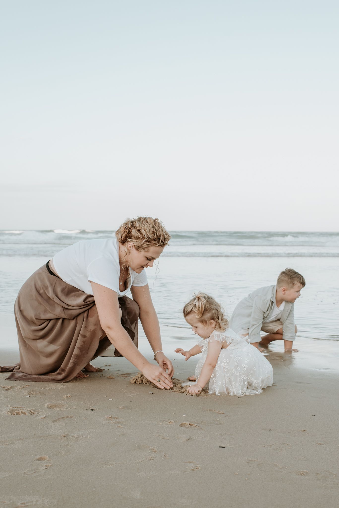A parent and children play together in the sand at the beach on an overcast day by the ocean.