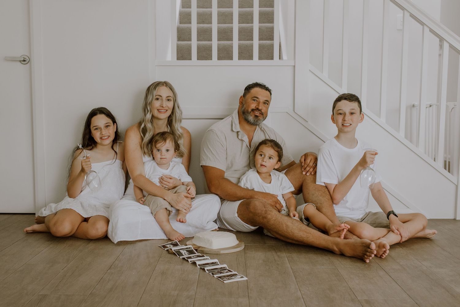 Family wearing white sits together on floor of bright modern home in casual lifestyle photography session.