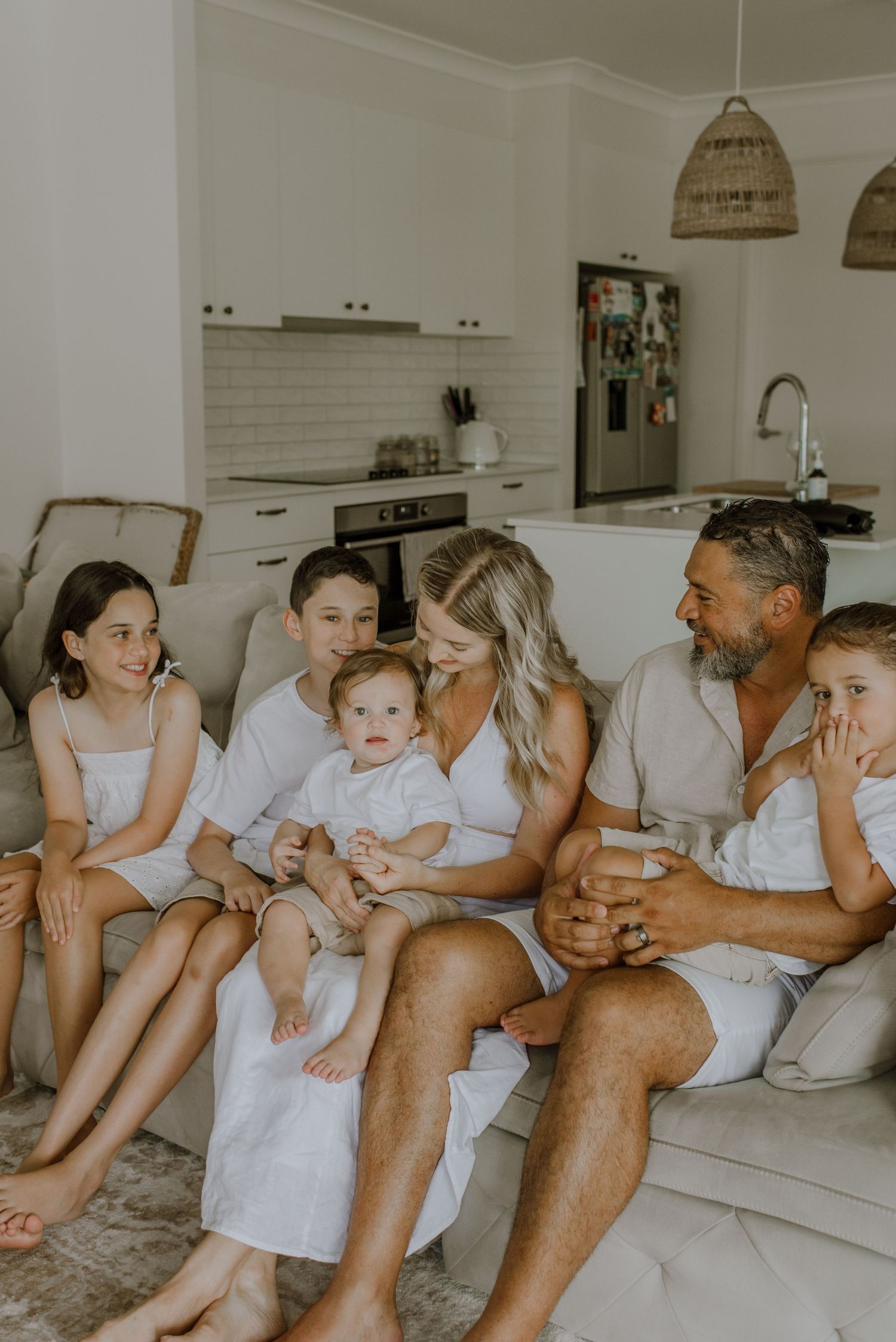 A family relaxes together on a white couch in a bright modern living room with coastal decor.