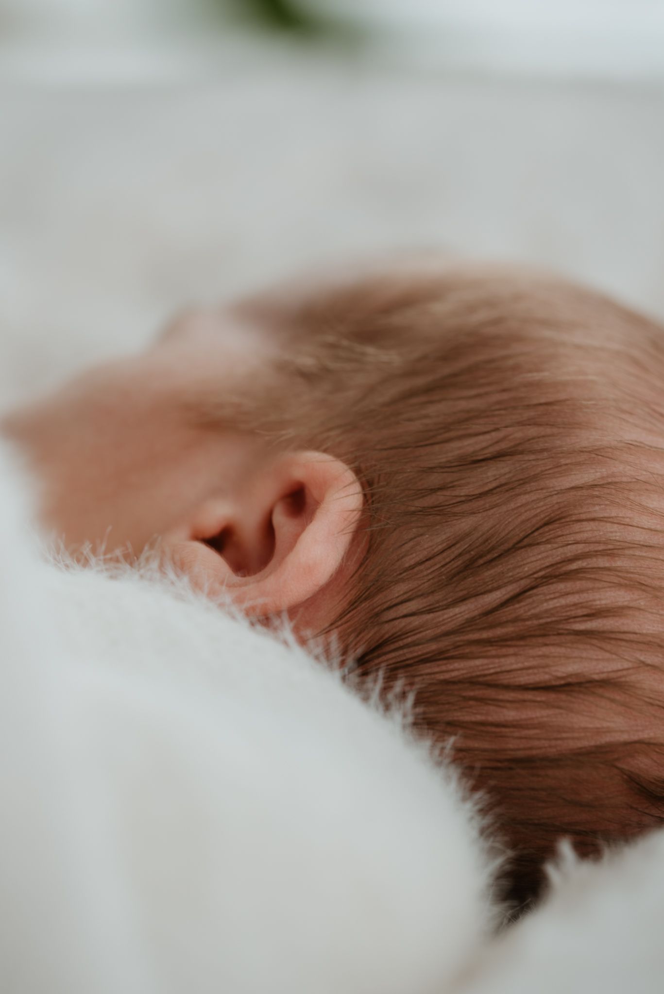 Close-up of a sleeping newborn baby with fine reddish-brown hair resting on a soft white blanket.