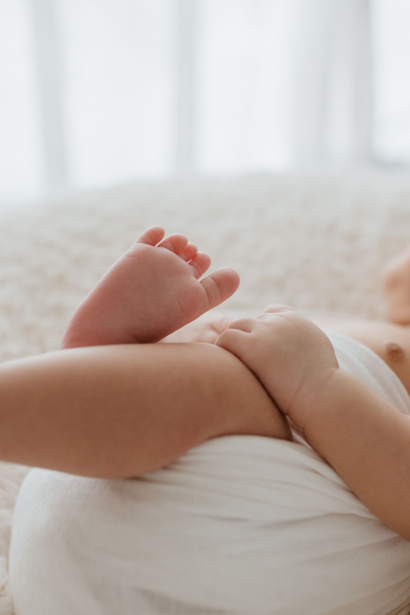 Close-up of tiny baby feet and legs resting on white fabric.