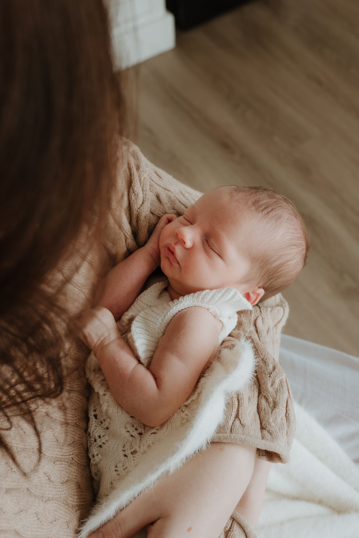 A sleeping newborn baby rests peacefully in a mother's arms, wrapped in a cozy knit blanket.