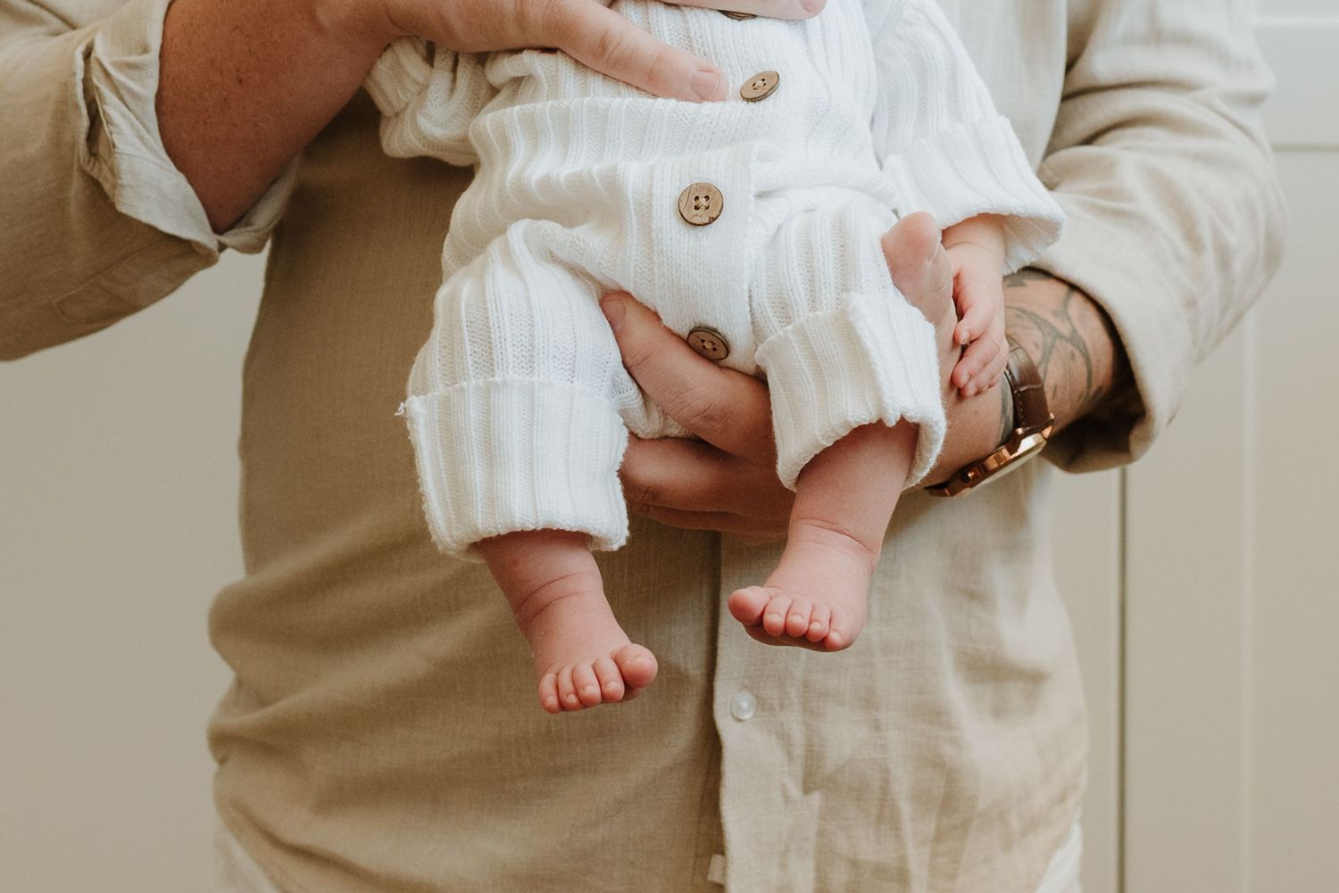 Close-up view of tiny baby feet and legs being held against soft white and beige clothing.
