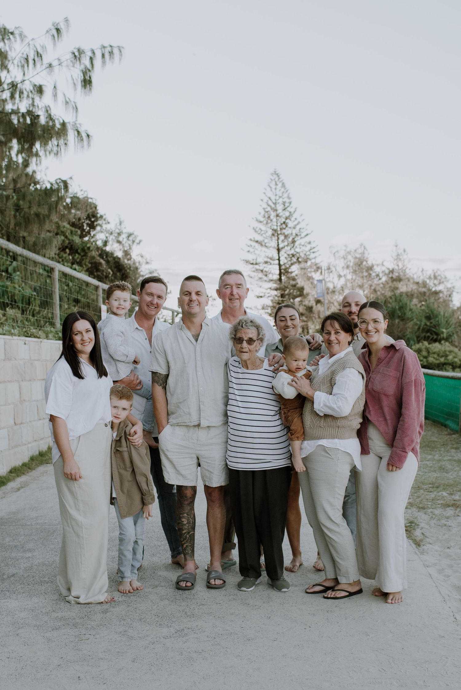 Multi-generational family group poses outdoors in coordinated white and neutral clothing on a sunny day.