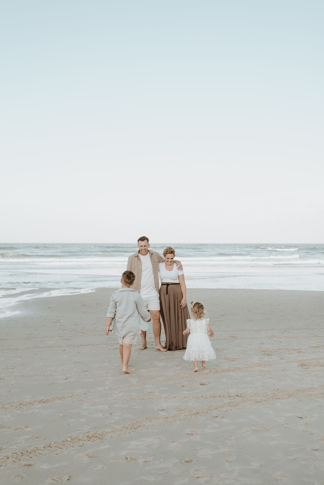 People walking together on a peaceful beach at sunset with soft muted tones and rolling waves in the background.
