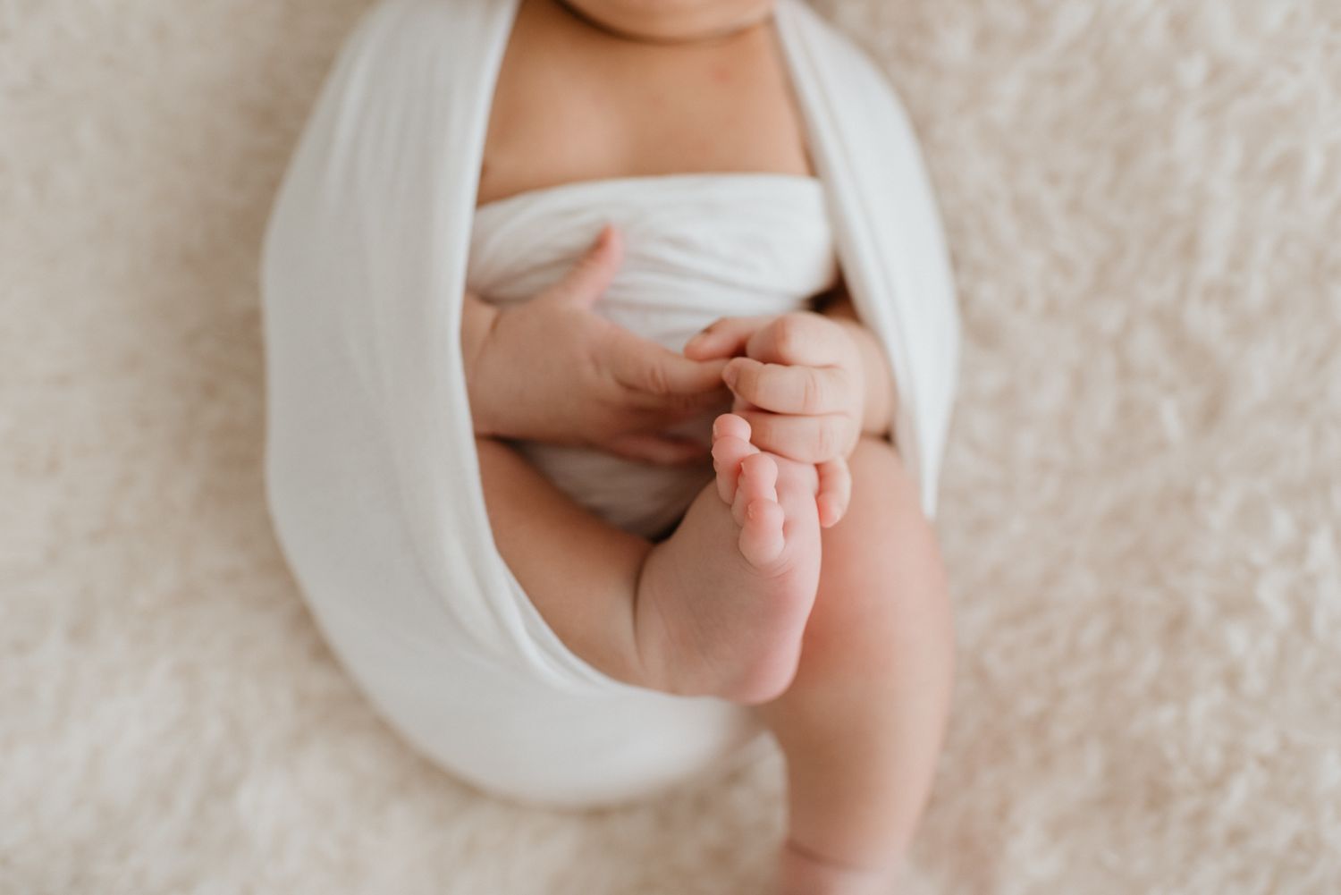 A tiny baby foot nestled in gentle hands against white fabric on a soft textured background.
